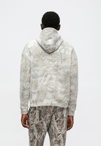 Felpa con cappuccio grigio chiaro con un motivo floreale testurizzato; presenta polsini e orlo a coste, abbinata a pantaloni dello stesso motivo.