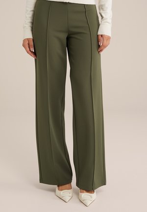 Pantaloni a gamba larga verde oliva realizzati in un tessuto liscio, con cuciture frontali e vita alta. Abbinati a tacchi bianchi a punta.