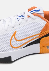 Hvide mesh-sneakers med orange accenter og sorte detaljer, der har et markant orange Nike-logo og en tekstureret gummisål.
