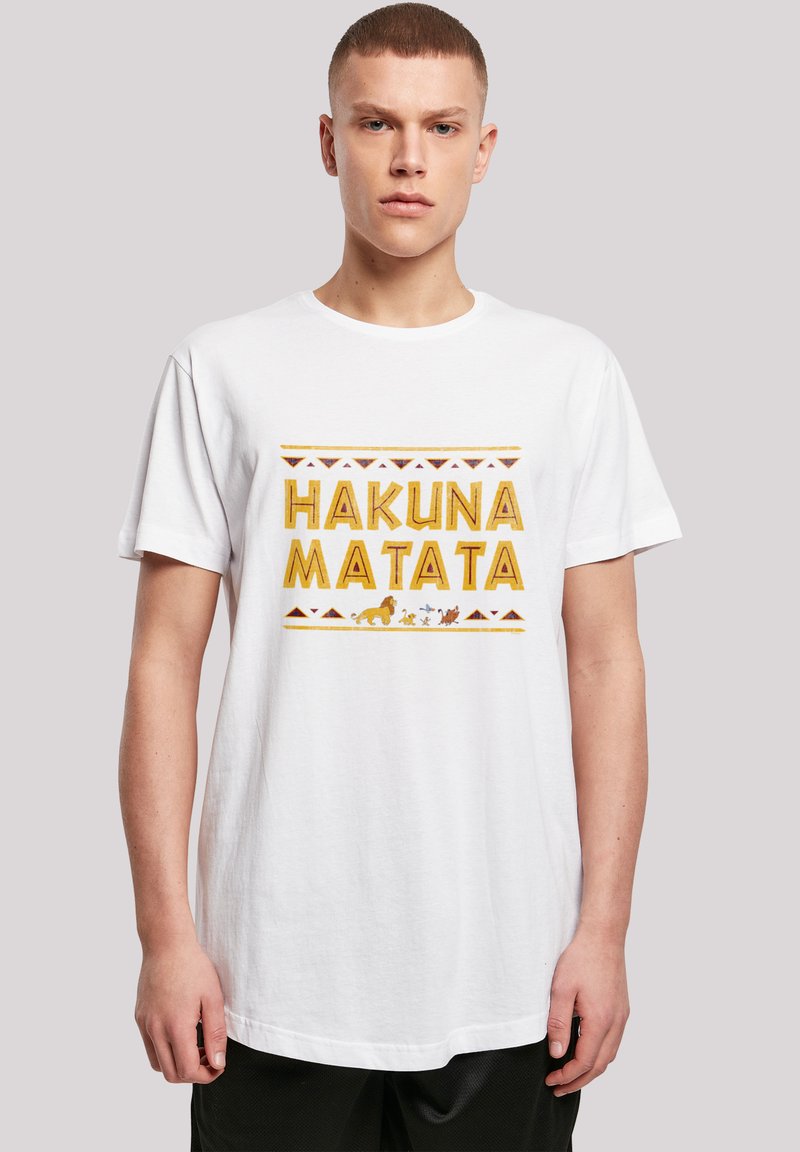 Bílé bavlněné tričko s nápisem "HAKUNA MATATA" tištěným tučnými žlutými písmeny, s grafickými obrázky zvířat a geometrickým vzorem v oranžové a hnědé barvě.