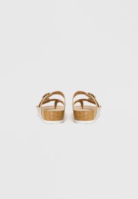 Καφέ πλατφόρμες σανδάλια από φελλό με δύο ρυθμιζόμενες ταινίες, λεία επάνω επιφάνεια και λευκή καουτσούκ σόλα. Η πίσω όψη αναδεικνύει το σχέδιο της φτέρνας και της ταινίας.