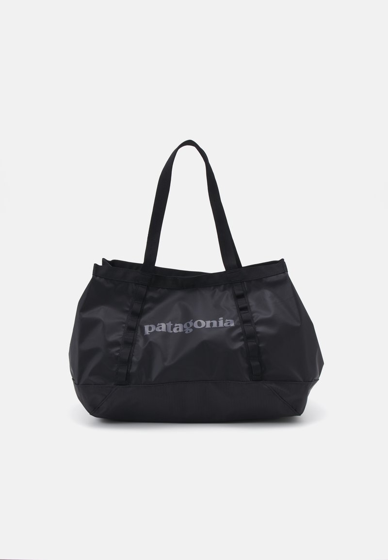 Črna torba iz trpežnega materiala z dvema zgornjima ročajema in izrazitim sivo "patagonia" logotipom spredaj; mehak tekstura, prilagodljiva oblika.