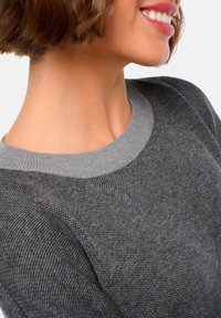 Grauer Strickpullover mit einem gerippten grauen Ausschnitt, der ein strukturiertes Muster aufweist. Der Stoff wirkt leicht und weich.
