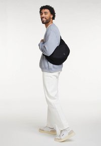 Borsa a tracolla nera con una finitura liscia, portata sulla spalla, abbinata a una felpa grigia chiara e pantaloni bianchi.