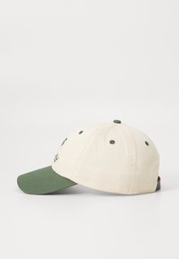 Baseballkasket i cremet bomuld med en grøn skygge. Den har broderet design og syningsdetaljer, seks ventilationshuller og en justerbar rem.