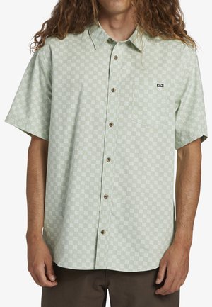 Kortærmet, button-up skjorte i lys grøn med et geometrisk hvidt mønster, der har en brystlomme og brune knapper.