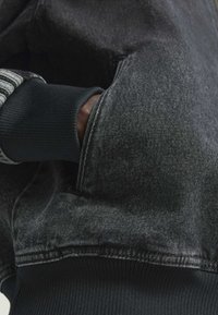 Crno denimsko dukserica s teksturiranom površinom, rebrastim manžetama i prednjim džepom s suptilnim izbljeđivanjem.