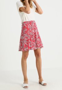 Gonna floreale rossa con un design a campana caratterizzata da motivi fogliari bianchi, realizzata in un tessuto morbido. Abbinata a una t-shirt bianca e sandali leggeri.