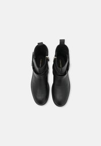 Botines de cuero negro con un acabado suave, cierre de cremallera y pequeños acentos decorativos en metal. Suela plana y forma de puntera redonda.