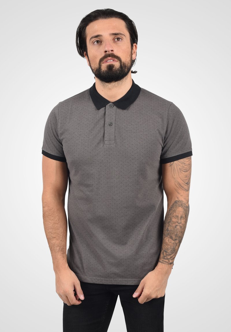 Polo gris à manches courtes, avec col noir et accents de manches. Présente un petit motif à pois, une patte de boutonnage à trois boutons et une coupe décontractée.