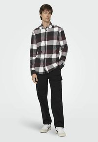 Camisa de cuadros en blanco y negro, de manga larga, combinada con pantalones cargo negros y zapatillas blancas. La camisa tiene un cuello clásico y un bolsillo.
