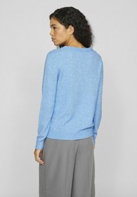 Šviesiai mėlynas megztinis, pagamintas iš minkštos medžiagos, su raukšlėta apačia ir rankogaliais. Dizainas apima platų iškirpimą ir laisvą siluetą.