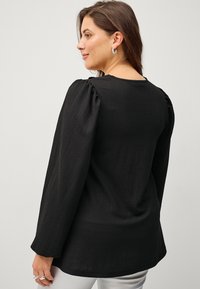 Black long-sleeve top with textured fabric and puffed shoulders. Features a round neckline and soft, relaxed fit. Simple, modern design.