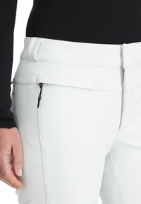 Weiße, enganliegende Hose mit glatter Textur, ausgestattet mit einer seitlichen Reißverschlusstasche und Gürtelschlaufen, konzipiert für einen maßgeschneiderten Look.