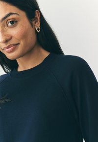 Marineblauwe sweatshirt met een geribbeld kraag en raglanmouwen, gecombineerd met gouden ringoorbellen. Glad materiaal met een minimalistisch ontwerp.