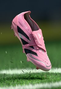 Roze voetbalschoen van synthetisch materiaal, met zwarte strepen en een gestructureerd oppervlak, voorzien van een klittenbandsluiting en verhoogde accenten.