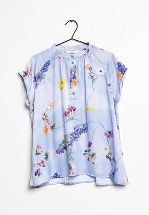 Lyseblå kortærmet bluse med flerfarvet blomsterprint, rund halsudskæring og treknapslukning, hængende på en sort bøjle.