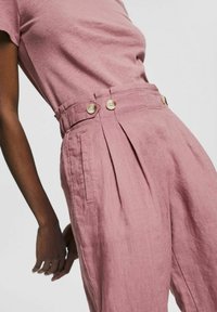 Roze linnen broek met plooien, zijzakken en twee decoratieve knopen op de tailleband; bijpassend top met korte mouwen. Zacht, gewatteerd materiaal.