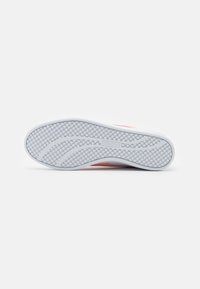Sole di sneaker in gomma bianca con una texture a motivo. Presenta un design liscio con un sottile logo PUMA e strisce laterali in tonalità rosa.