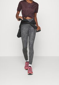 Camiseta ajustada de color púrpura oscuro con dobladillo retorcido, combinada con leggings grises texturizados de tiro alto y zapatillas deportivas rosas. Chaqueta negra atada a la cintura.