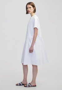 Witte, korteblaadige jurk met een gelaagde rok, met een losse pasvorm en zachte textuur. Draag het met zwart-witte open-toe sandalen.