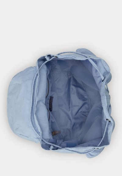Mochila de tela azul claro con parte superior abierta, forro interior visible, bolsillo con cremallera y etiqueta "Polo Ralph Lauren" en el interior.