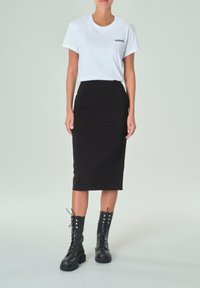 Camiseta blanca con un pequeño logo negro, combinada con una falda lápiz negra de talle alto y botas negras hasta la rodilla con cordones.