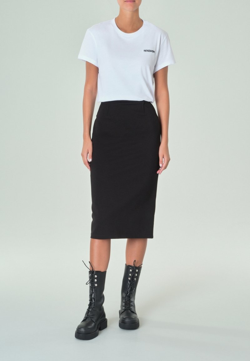 Camiseta blanca con un pequeño logo negro, combinada con una falda lápiz negra de talle alto y botas negras hasta la rodilla con cordones.