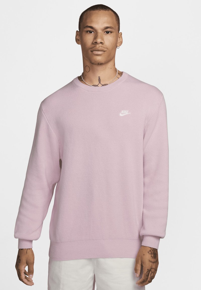 Jasnoróżowy sweter dzianinowy z okrągłym dekoltem, ściągaczami przy mankietach i dolnej krawędzi, z małym białym logo Nike na piersi.