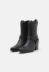 Black leather ankle boots feature a block heel, rounded toe, and a decorative strap with metal accents. Zipper closure at the back.