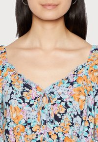 Vestido floral com fundo azul-marinho e flores em laranja e azul-claro. Decote em babados com detalhe de laço à frente. Mangas curtas.