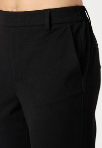 Pantalons noirs ajustés en tissu doux et texturé, avec une taille plate, des poches latérales et une bande de taille partiellement élastique pour plus de confort.