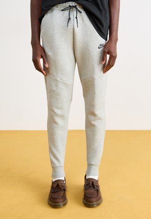 Gray sweatpants with a drawstring waist, tapered legs, and stitched panel details, paired with brown shoes and white socks.
