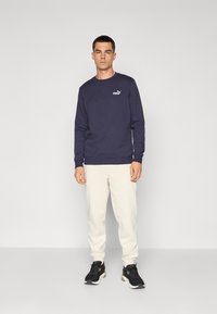 Navy blue sweatshirt with crew neckline and small white Puma logo, paired with cream-colored sweatpants and black athletic shoes.
