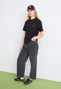 Black cotton t-shirt, loose fit, front graphic. Gray denim pants, wide-leg design. Black sneakers with subtle detailing and white accents.