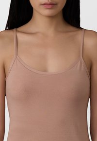Top senza maniche color nude con sottili spalline, realizzato in un morbido tessuto elasticizzato. Presenta un scollo basso e una texture liscia priva di decorazioni.