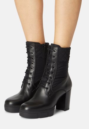 Svarta ankelstövlar med en kombination av slätt läder och quiltat tyg, snörning framtill och klumpiga höga klackar.