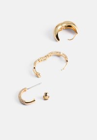 Boucles d'oreilles dorées avec divers designs : un croissant lisse, une chaîne reliée et une pièce courbée avec de petits gemmes clairs, ainsi qu'un crochet et un support.
