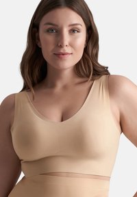 Bralette beige senza cuciture con scollatura a V, spalline larghe e tessuto morbido e elastico. Presenta una superficie liscia e dettagli a coste sottili al centro.