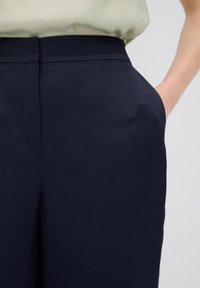 Marina byxor med en mjuk yta, vida ben och sidofickor. Har en ren design på midjebandet, kompletterat av en ljusblommig blus.