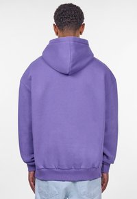Lilla hættejakke med en afslappet pasform, blød tekstur, ribbede manchetter og kant. Har en stor hætte og minimalistisk design.