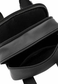 Svart syntetisk ryggsäck med två dragkedjeförsedda fack och tygremmar, med en slät yta och minimalistisk design.