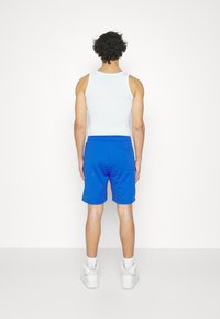 White tank top with blue shorts; shorts feature an elastic waistband, side pockets, and smooth texture, worn with white sneakers.