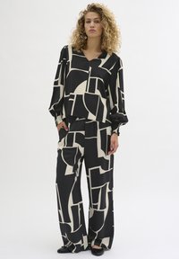 Black and beige two-piece outfit featuring a loose V-neck top with balloon sleeves and wide-leg trousers, both with a geometric pattern.