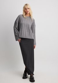 Gray knitted sweater with a cable pattern, paired with a long black pinstriped skirt and black chunky loafers. Soft texture, relaxed fit.