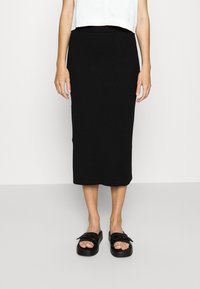 Černá midi sukně z vroubkované pleteniny s přiléhavým pasem, v kombinaci s černými slip-on botami s širokým páskem. Bílý zkrácený top nahoře.