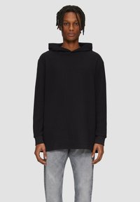 Zwarte hoodie van zacht materiaal, met een kangoeroezak, lange mouwen en een relaxed fit. Gecombineerd met lichtgrijze distressed jeans.