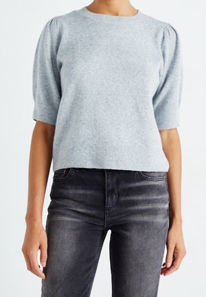 Světlounce šedý krátký svetr z měkkého úpletu, s kulatým výstřihem, žebrovaným lemem a jemně nafouklými rukávy, v kombinaci s tmavými džínami.