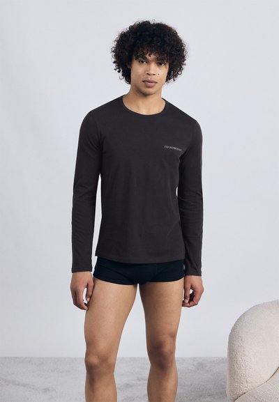 Camisa preta de manga longa feita de tecido macio, com gola redonda e pequeno detalhe do logo no peito, combinada com calções pretos.