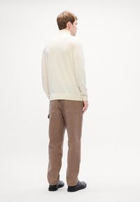 Pulover crem cu o croială lejeră și manșete ribbrate, asortat cu pantaloni cargo maron cu două buzunare pe spate. Textură netedă, design minimal.